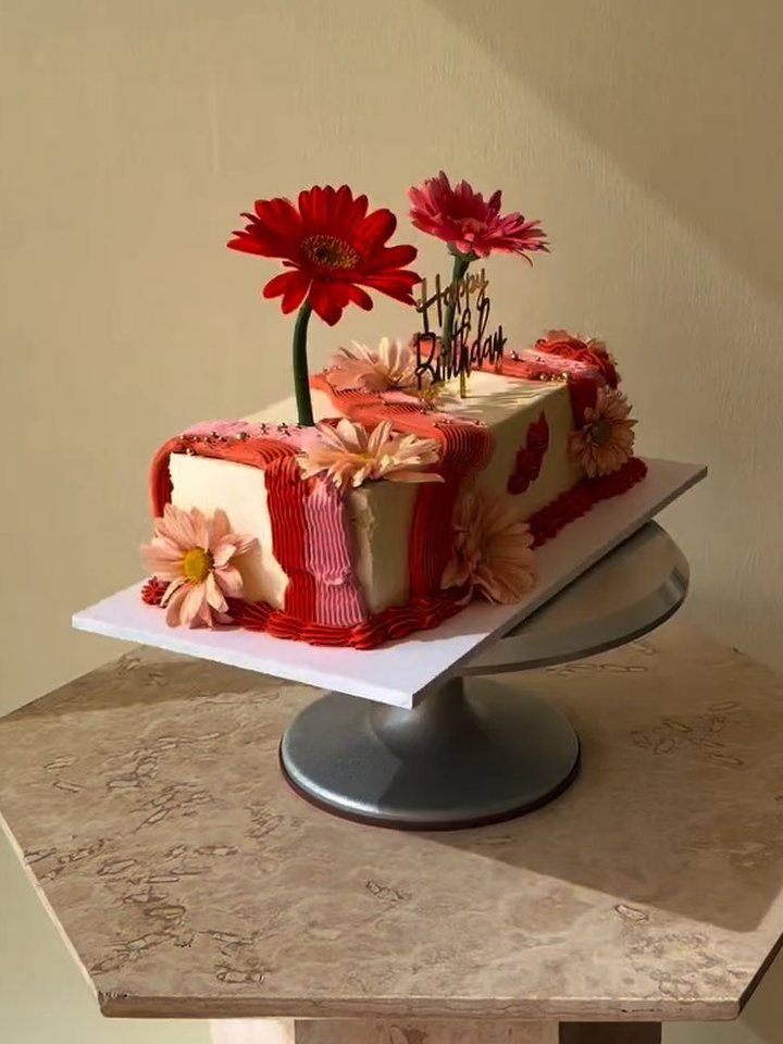 Long cake de buttercream con franjas rojas, gerberas naturales y topper dorado de Happy Birthday